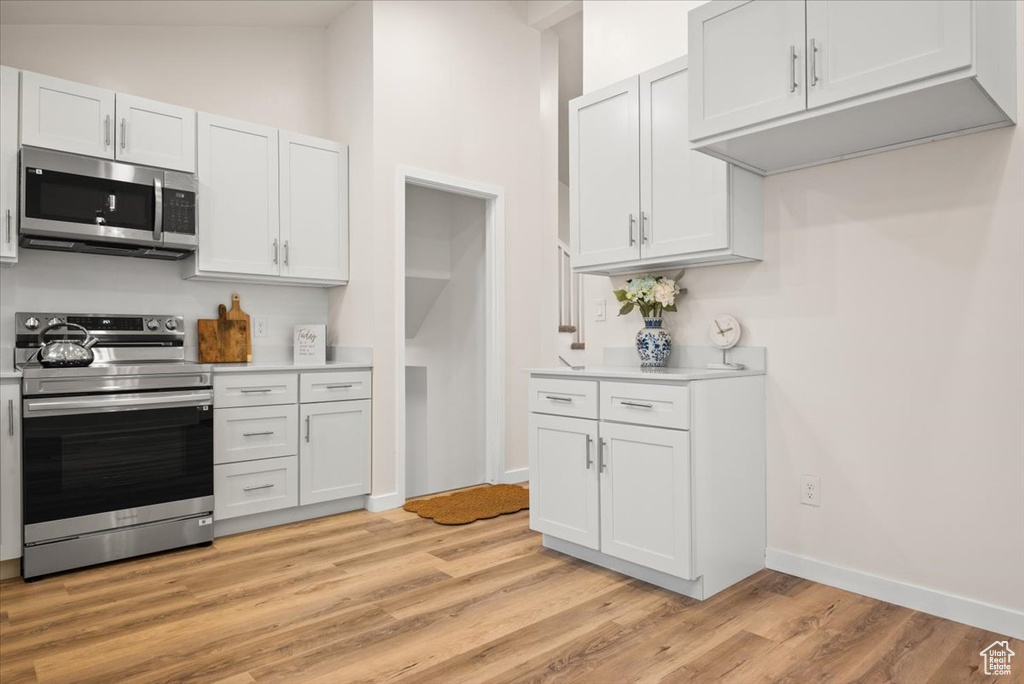 Kitchen with white cabinetry, high vaulted ceiling, stainless steel appliances, and light hardwood / wood-style flooring