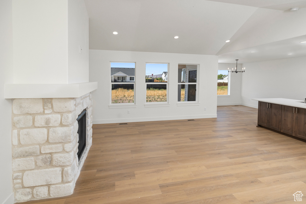 Unfurnished living room with a fireplace, light hardwood / wood-style flooring, lofted ceiling, and a chandelier