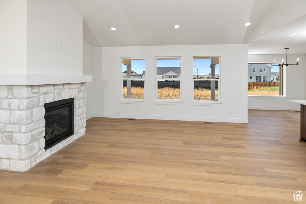 Unfurnished living room featuring light hardwood / wood-style floors, vaulted ceiling, an inviting chandelier, and a fireplace