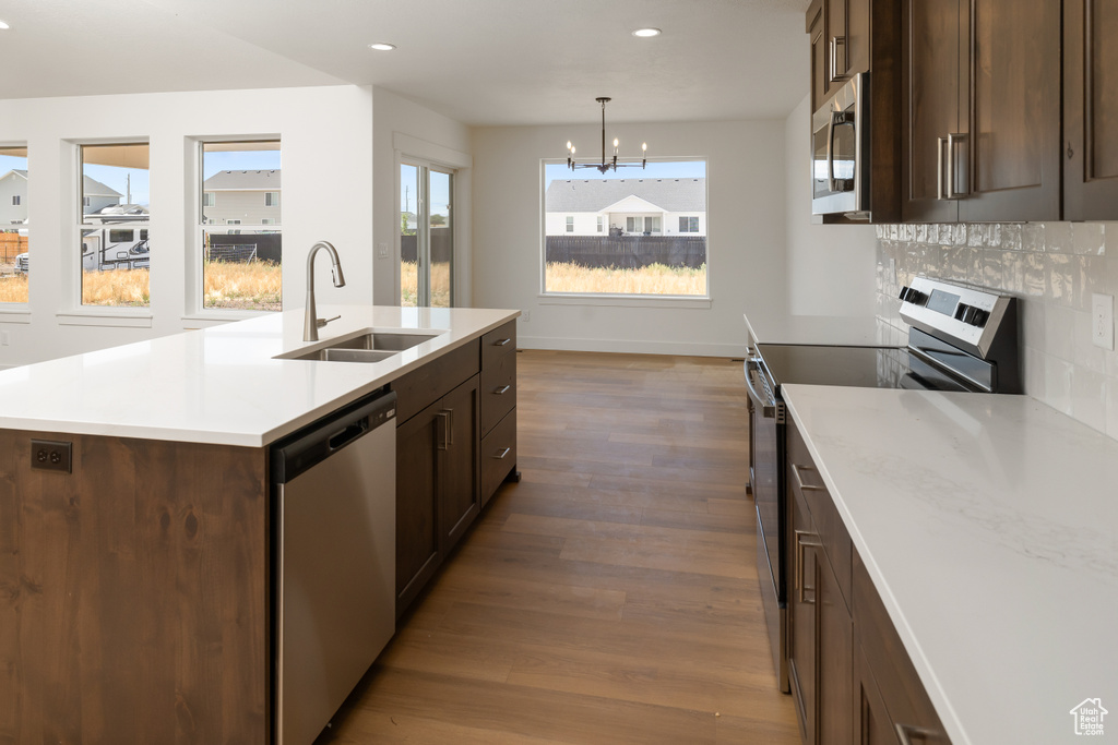 Kitchen with hardwood / wood-style floors, backsplash, sink, appliances with stainless steel finishes, and hanging light fixtures