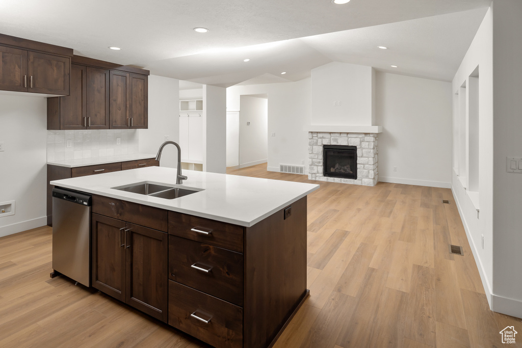 Kitchen featuring light wood-type flooring, backsplash, dishwasher, sink, and a fireplace