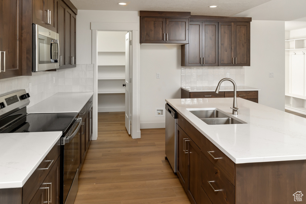 Kitchen featuring stainless steel appliances, light hardwood / wood-style flooring, decorative backsplash, sink, and a kitchen island with sink