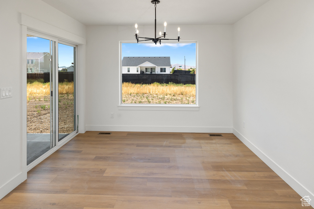 Unfurnished dining area with light hardwood / wood-style flooring, a healthy amount of sunlight, and an inviting chandelier