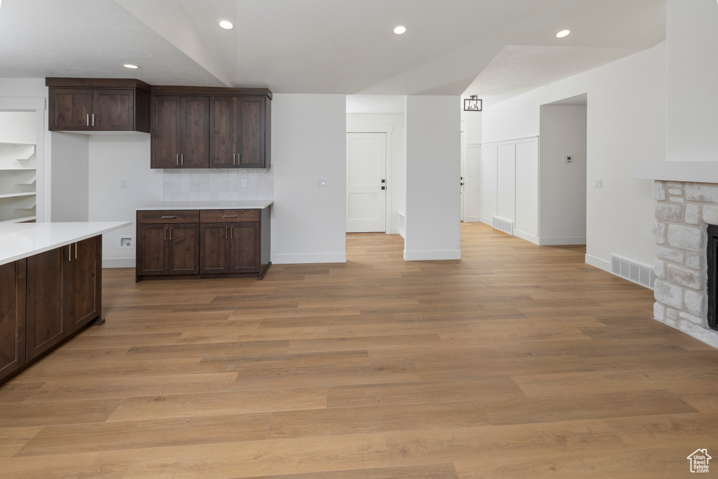 Kitchen with a fireplace, light hardwood / wood-style floors, tasteful backsplash, and dark brown cabinets