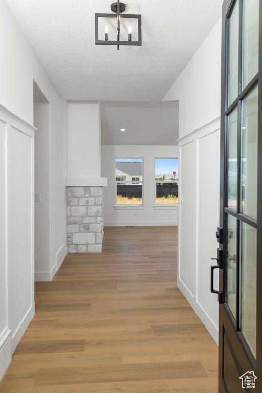 Hall with light wood-type flooring, a textured ceiling, and a chandelier