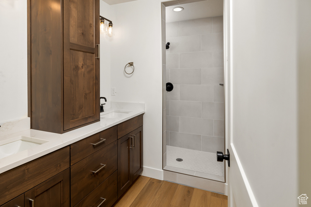 Bathroom with hardwood / wood-style floors, double vanity, and tiled shower