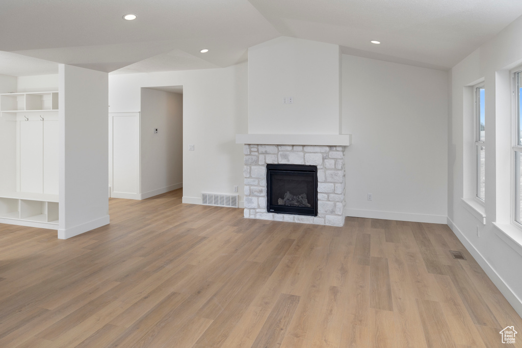 Unfurnished living room featuring light wood-type flooring, vaulted ceiling, and a stone fireplace