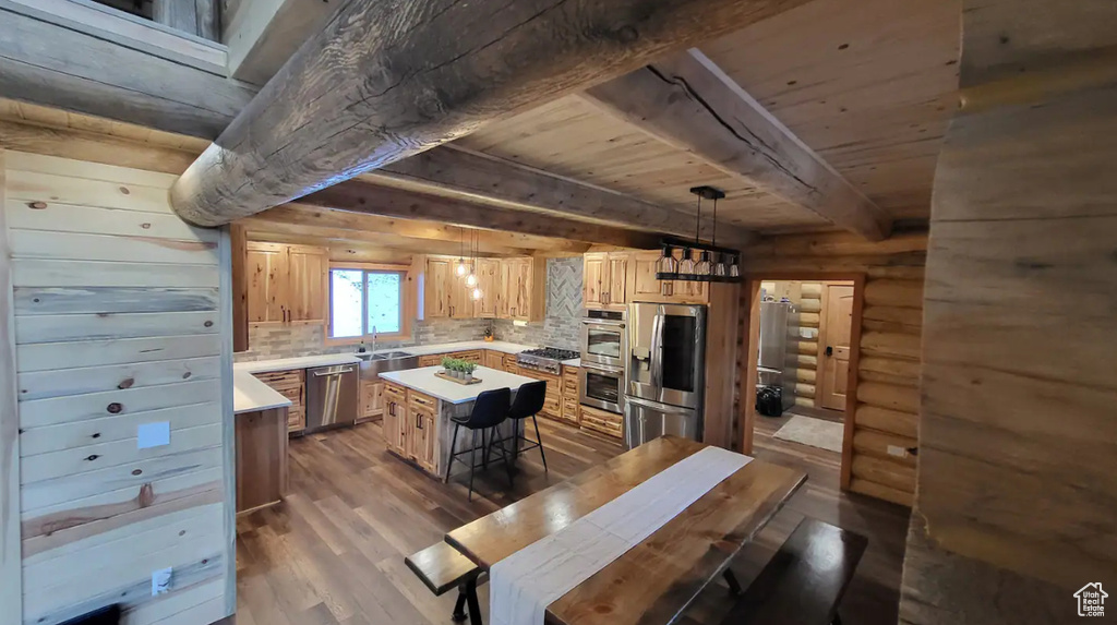 Kitchen featuring decorative light fixtures, stainless steel appliances, decorative backsplash, wood-type flooring, and a center island