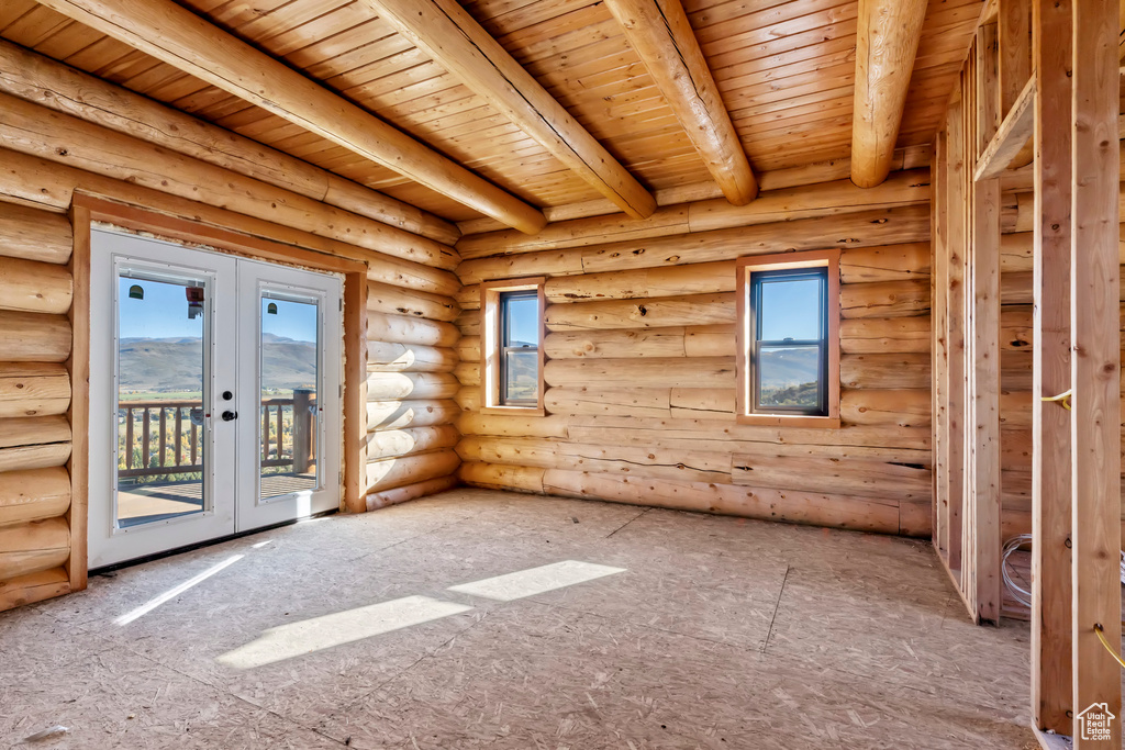 Empty room with log walls, wooden ceiling, beamed ceiling, and french doors