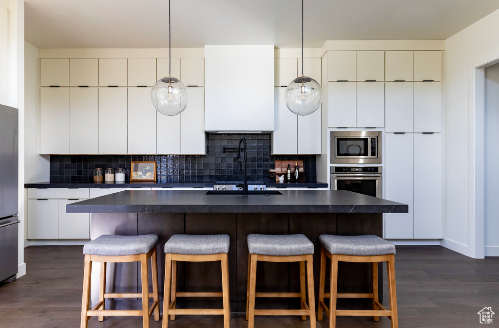 Kitchen with decorative backsplash, appliances with stainless steel finishes, dark hardwood / wood-style floors, and a center island