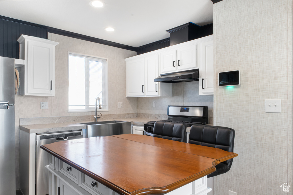 Kitchen featuring sink, a kitchen bar, white cabinetry, and stainless steel appliances