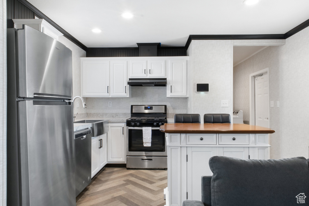 Kitchen with light parquet flooring, white cabinets, sink, crown molding, and stainless steel appliances