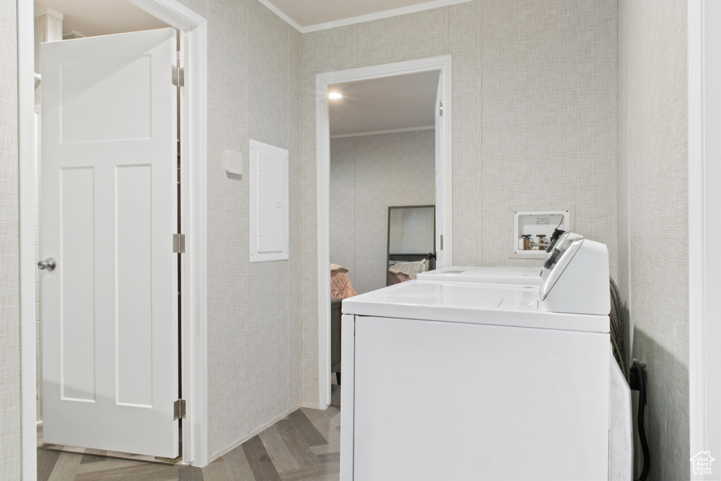 Clothes washing area with washing machine and dryer, electric panel, crown molding, and light wood-type flooring