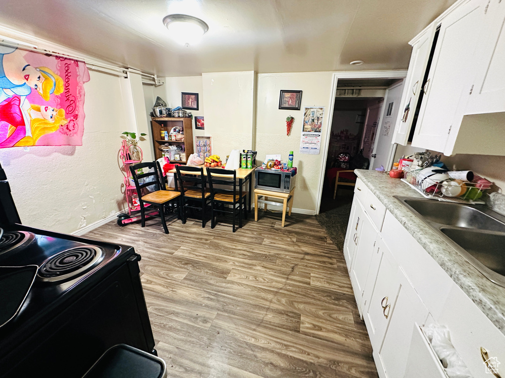 Kitchen featuring white cabinetry, sink, light hardwood / wood-style flooring, and stainless steel microwave