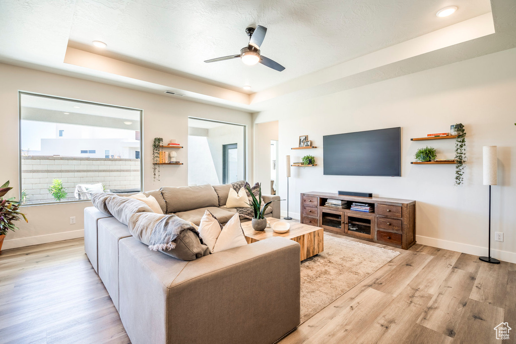 Living room with a tray ceiling, ceiling fan, and light wood-type flooring