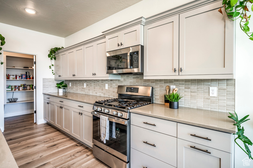 Kitchen featuring decorative backsplash, light hardwood / wood-style flooring, gray cabinetry, appliances with stainless steel finishes, and light stone counters