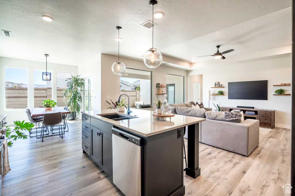 Kitchen with sink, decorative light fixtures, light hardwood / wood-style flooring, an island with sink, and stainless steel dishwasher