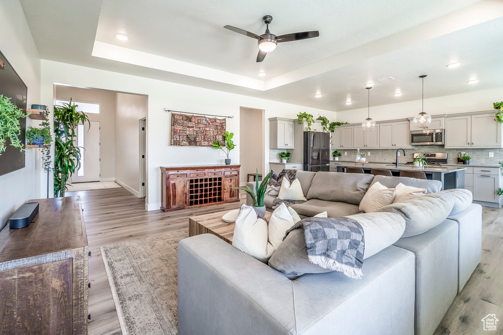 Living room with a tray ceiling, light hardwood / wood-style flooring, ceiling fan, and sink