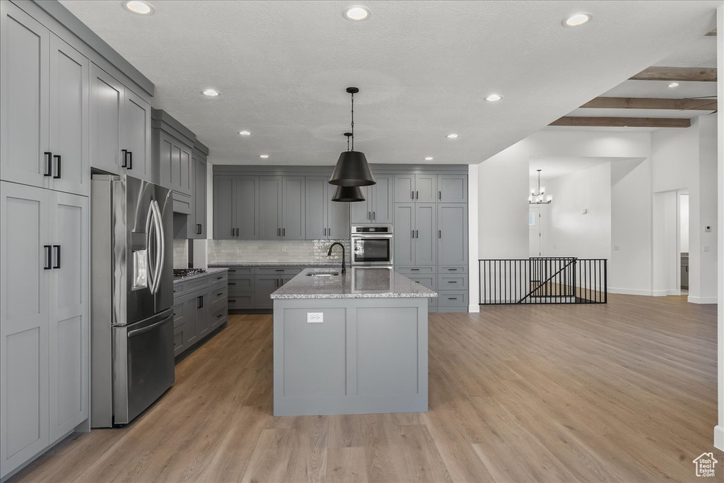 Kitchen with stainless steel appliances, light hardwood / wood-style flooring, tasteful backsplash, beamed ceiling, and a kitchen island with sink