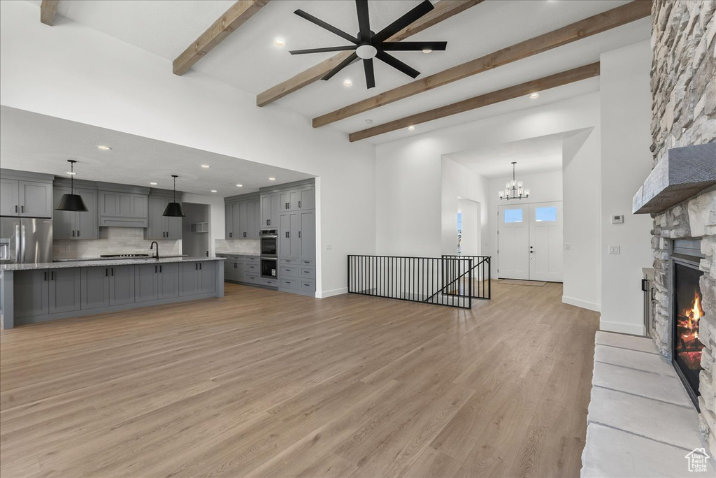 Living room with a high ceiling, a fireplace, beamed ceiling, light hardwood / wood-style flooring, and ceiling fan with notable chandelier