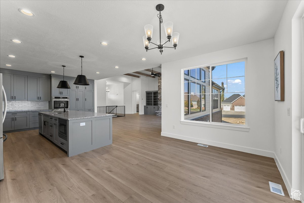 Kitchen featuring light hardwood / wood-style flooring, light stone counters, a center island with sink, stainless steel oven, and gray cabinets