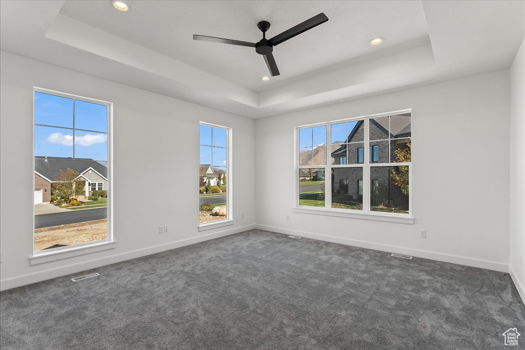 Unfurnished room featuring ceiling fan, dark carpet, and a tray ceiling