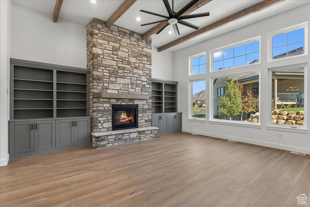 Unfurnished living room with ceiling fan, light hardwood / wood-style flooring, a towering ceiling, a fireplace, and beamed ceiling