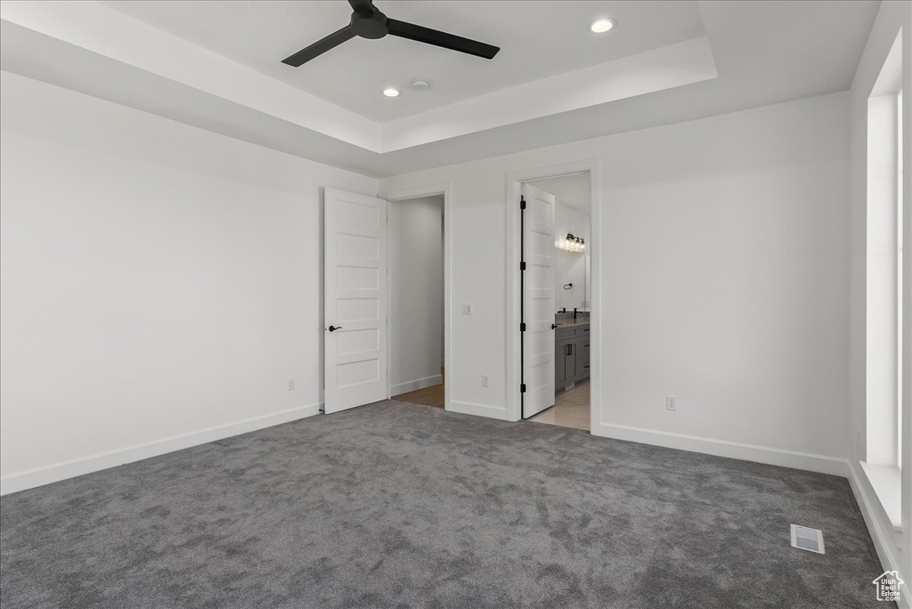 Unfurnished bedroom featuring ceiling fan, a raised ceiling, connected bathroom, and carpet floors