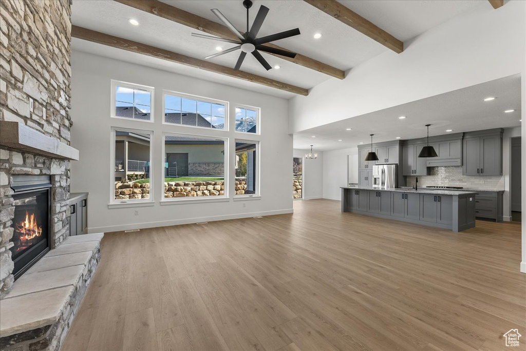 Unfurnished living room with a stone fireplace, beamed ceiling, light hardwood / wood-style floors, a towering ceiling, and ceiling fan