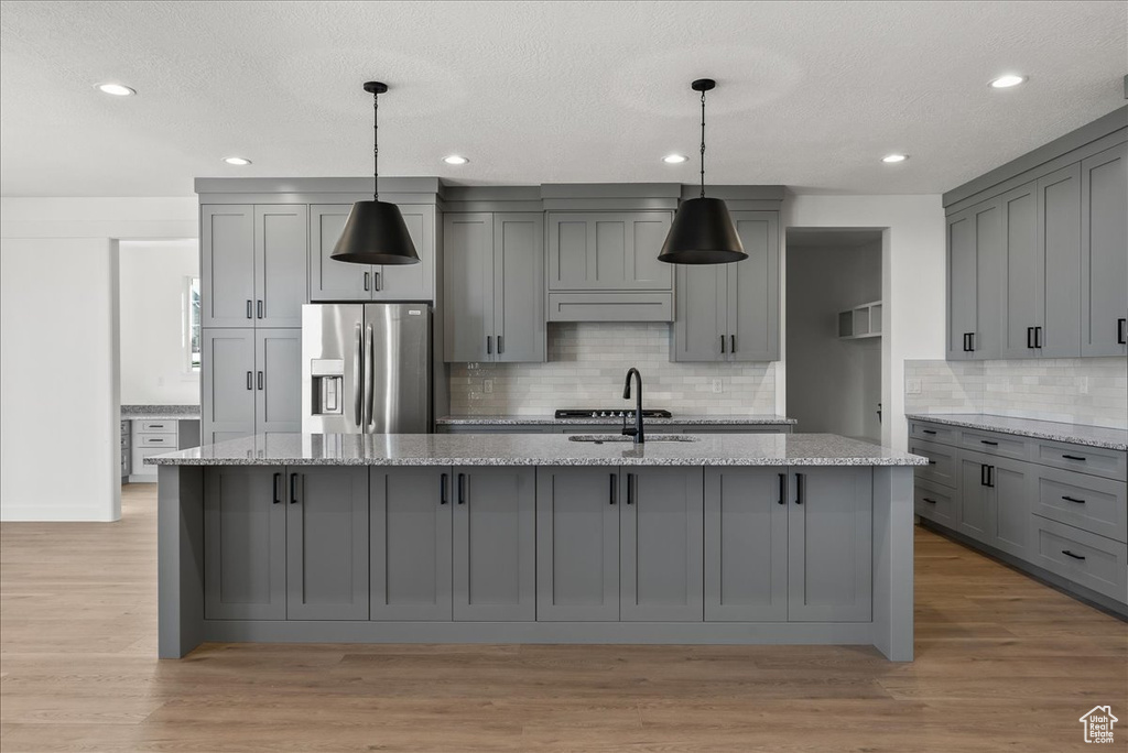 Kitchen with gray cabinetry, stainless steel fridge, light stone counters, and light hardwood / wood-style floors