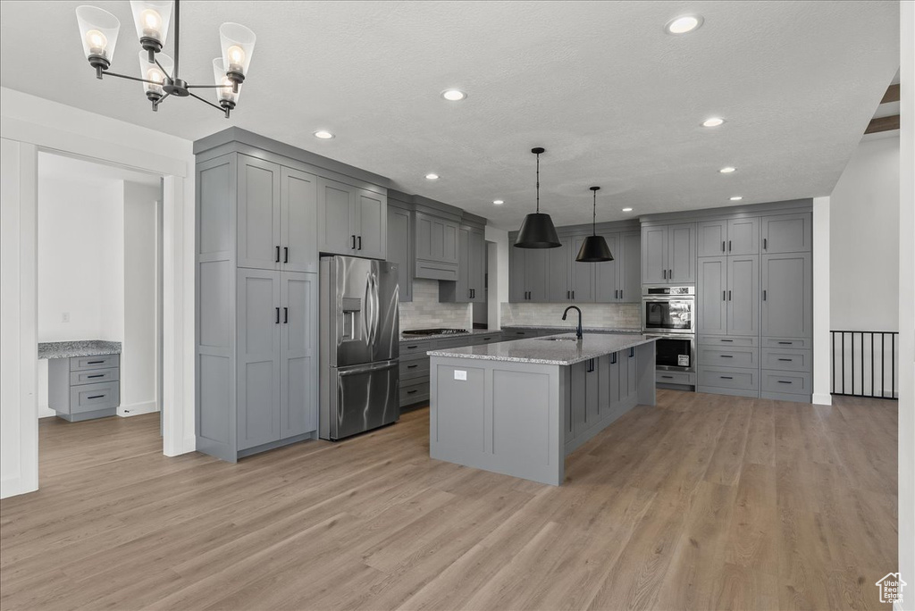 Kitchen featuring pendant lighting, a kitchen island with sink, appliances with stainless steel finishes, light stone counters, and light hardwood / wood-style floors