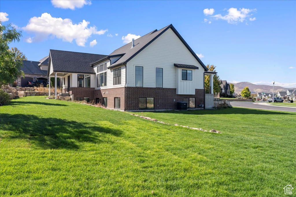 Back of property with central AC unit, a yard, and a mountain view