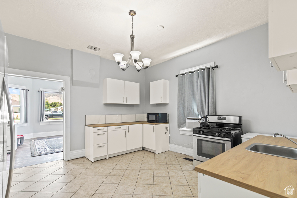 Kitchen featuring decorative light fixtures, a notable chandelier, white cabinets, light tile patterned floors, and stainless steel range with gas cooktop