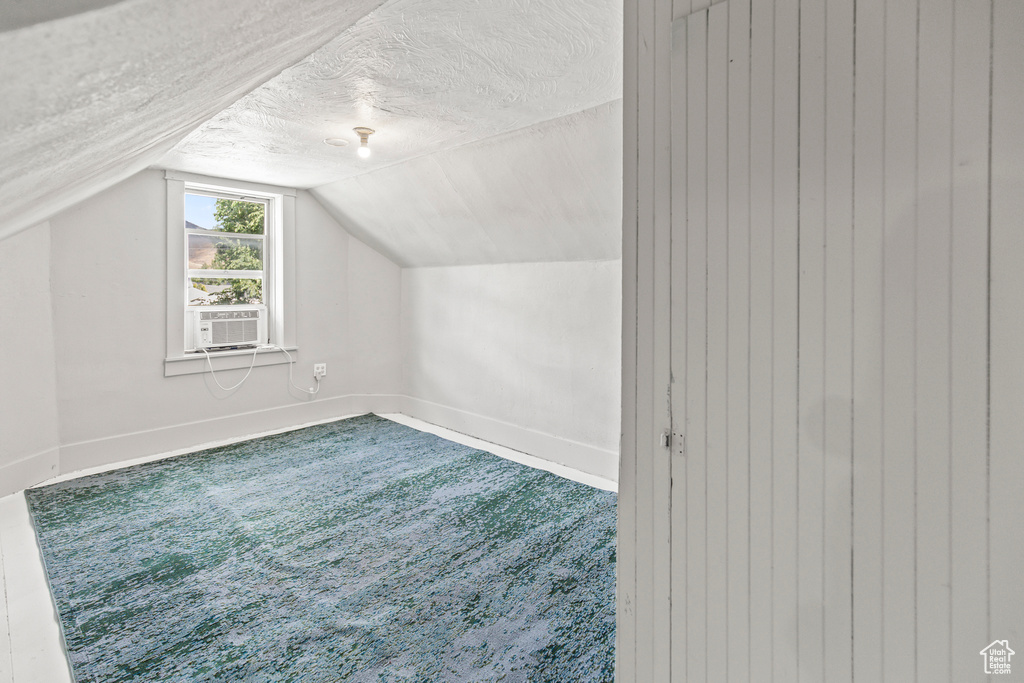 Additional living space with a textured ceiling, cooling unit, and lofted ceiling