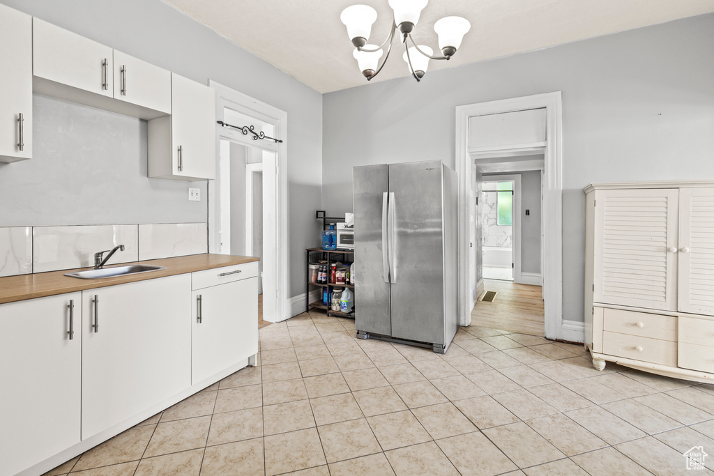 Kitchen featuring sink, light hardwood / wood-style flooring, a chandelier, stainless steel refrigerator, and white cabinetry