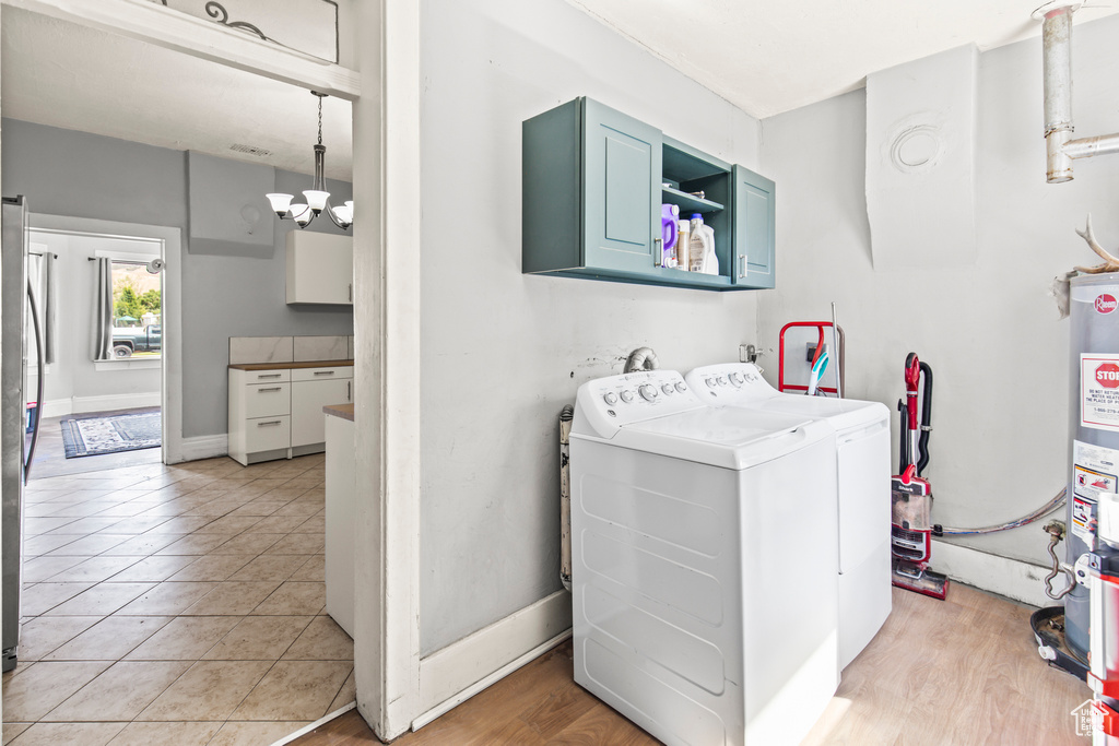 Clothes washing area with light hardwood / wood-style floors, washing machine and clothes dryer, a notable chandelier, and cabinets