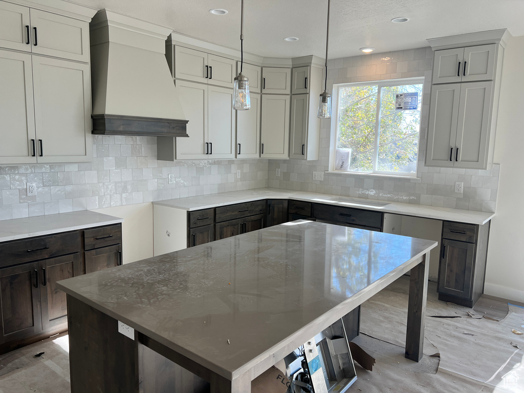 Kitchen featuring custom exhaust hood, gray cabinets, a kitchen island, backsplash, and pendant lighting