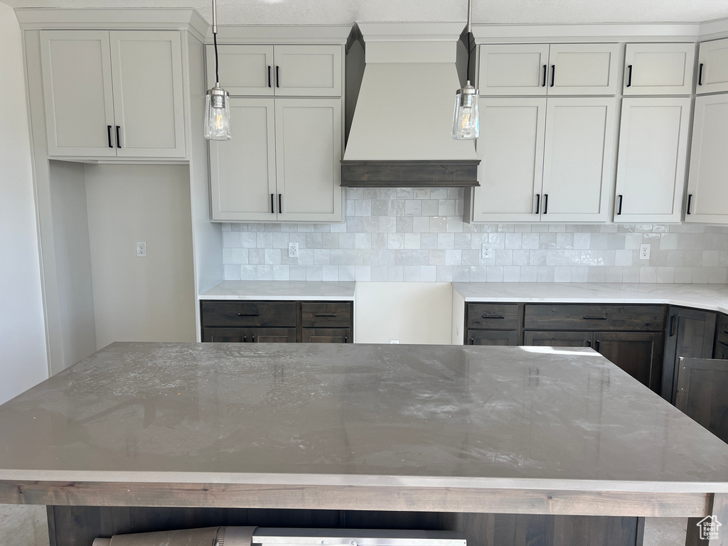 Kitchen with custom range hood, decorative light fixtures, light stone counters, and tasteful backsplash