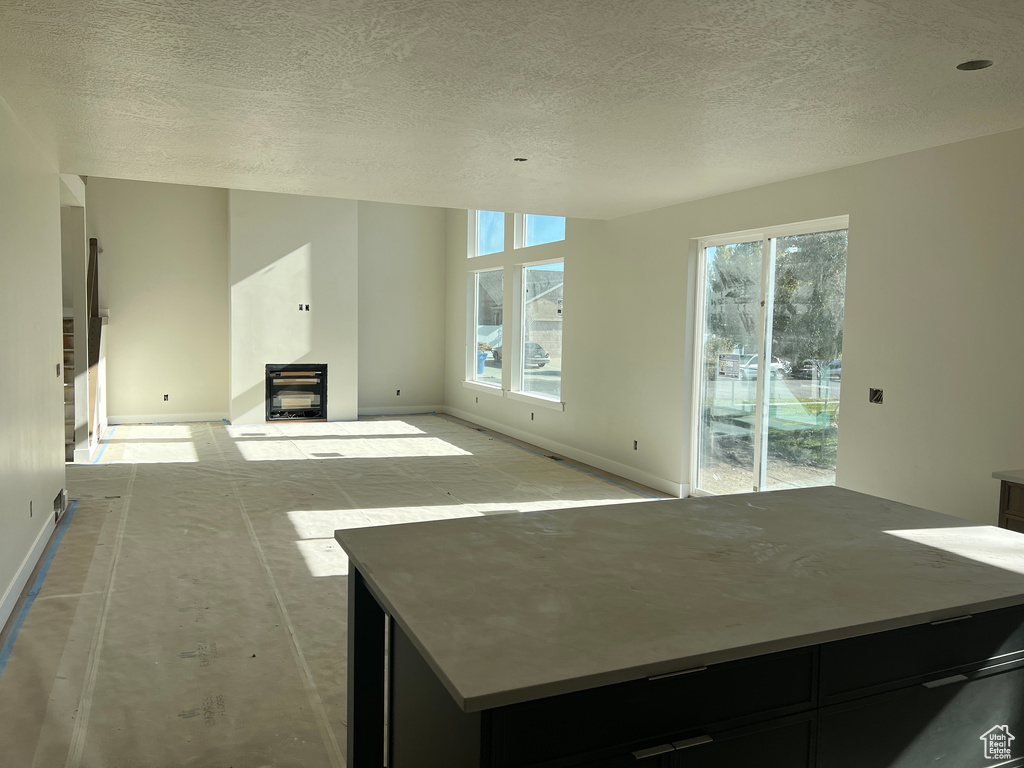 Unfurnished living room featuring a wealth of natural light, a wood stove, and a textured ceiling