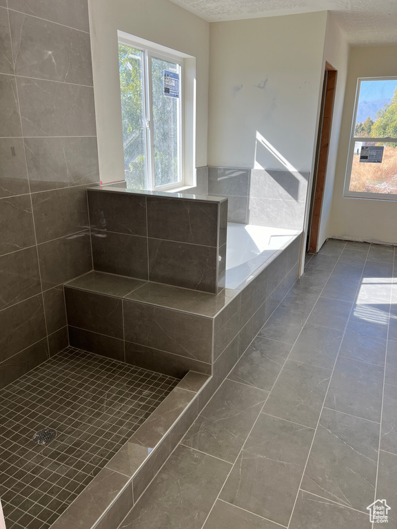 Bathroom with shower with separate bathtub, plenty of natural light, tile patterned flooring, and a textured ceiling