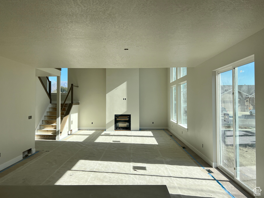 Unfurnished living room featuring a textured ceiling, a healthy amount of sunlight, and a wood stove