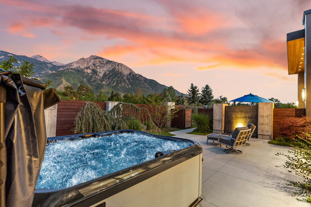 Pool at dusk featuring a mountain view, a hot tub, and a patio area