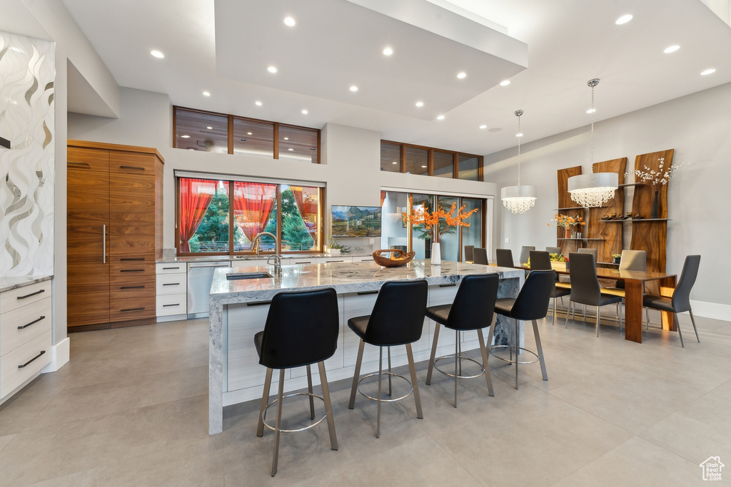 Kitchen featuring stainless steel dishwasher, a large island with sink, light stone counters, and light tile patterned floors