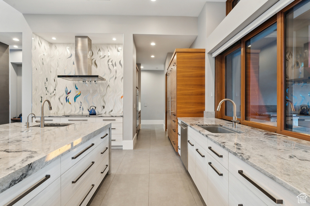 Kitchen featuring appliances with stainless steel finishes, island range hood, sink, light stone countertops, and light tile patterned floors