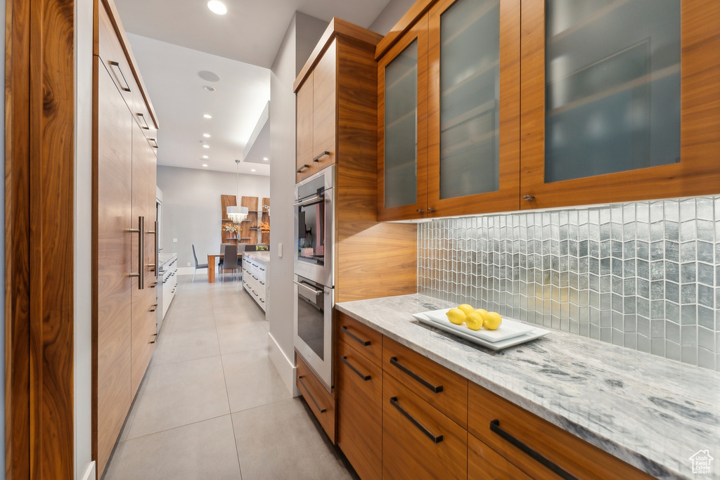 Kitchen with light tile patterned floors, stainless steel double oven, decorative backsplash, and light stone counters