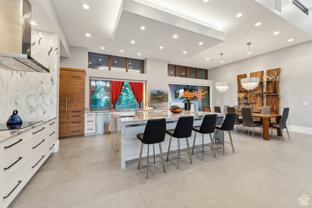 Kitchen with wall chimney exhaust hood, hanging light fixtures, a large island, dishwasher, and light tile patterned floors