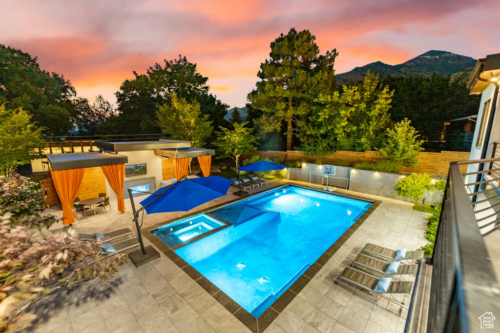 Pool at dusk featuring an in ground hot tub, a mountain view, and a patio area