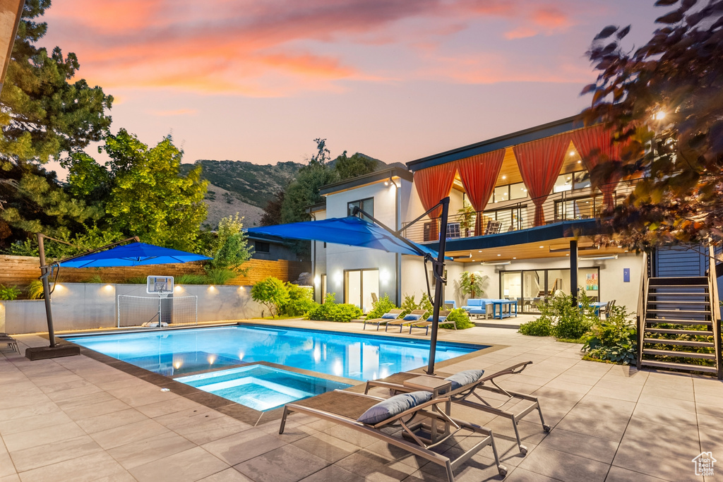 Pool at dusk with an in ground hot tub and a patio