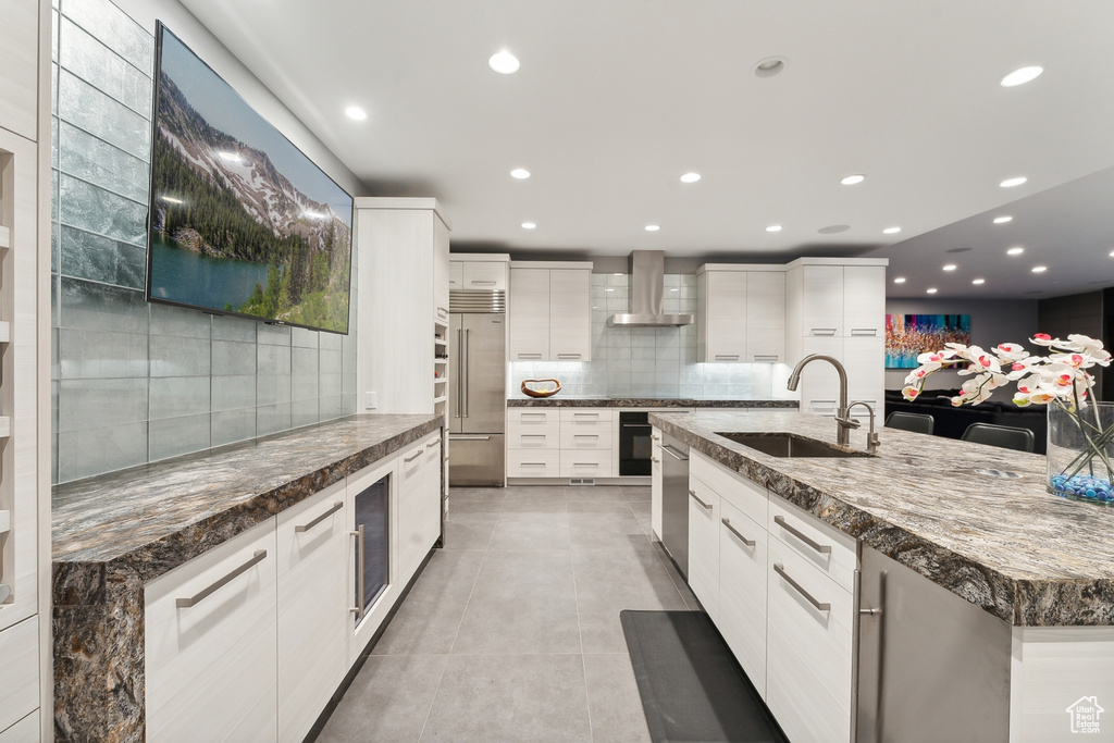 Kitchen featuring light tile patterned flooring, sink, wall chimney exhaust hood, and a spacious island