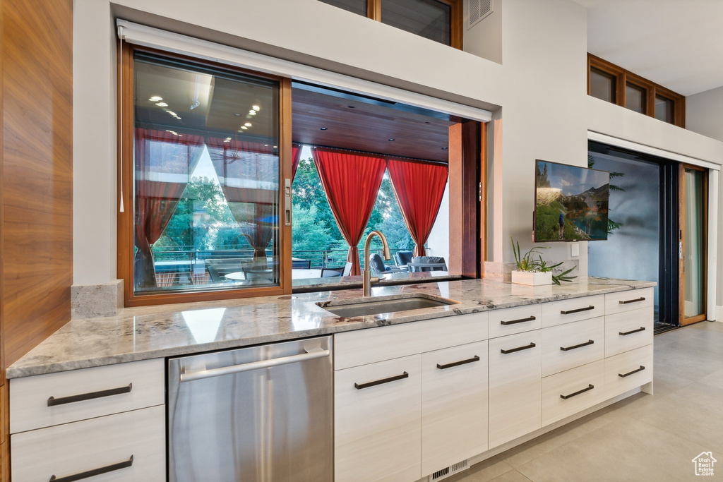 Kitchen with sink, dishwasher, light stone countertops, and light tile patterned floors